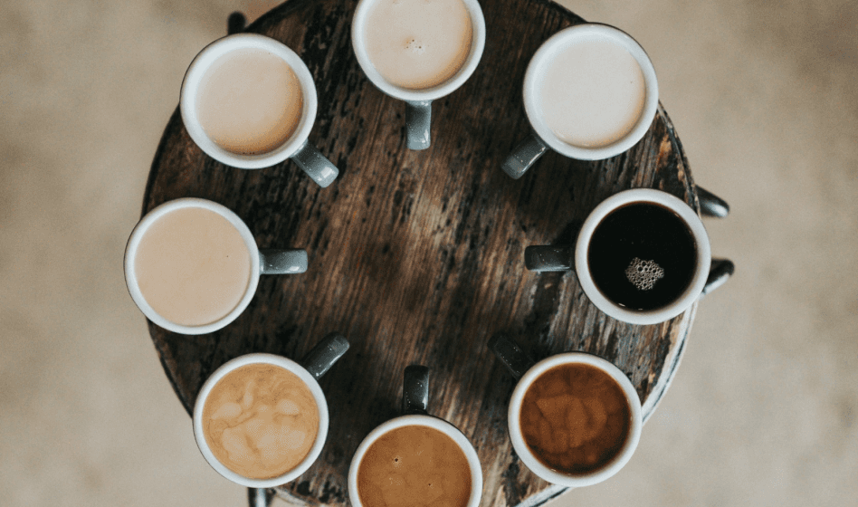 Round table with eight colorful coffee cups arranged in a circle, set against a blurred floor.