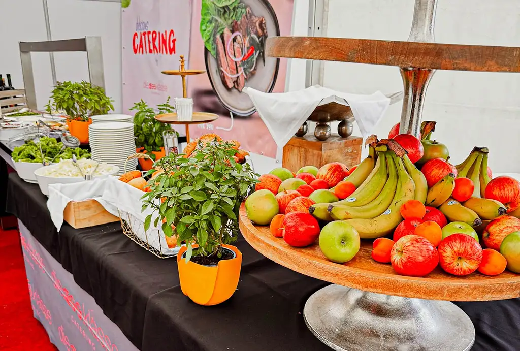 A vibrant table setting featuring burgers, hot dogs, fries, and colorful drinks, illuminated by string lights.
