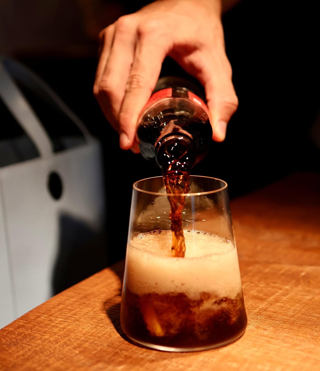 Cola wird in ein Glas eingeschenkt und bildet eine schaumige Oberfläche auf einer Holztheke im kAlps.