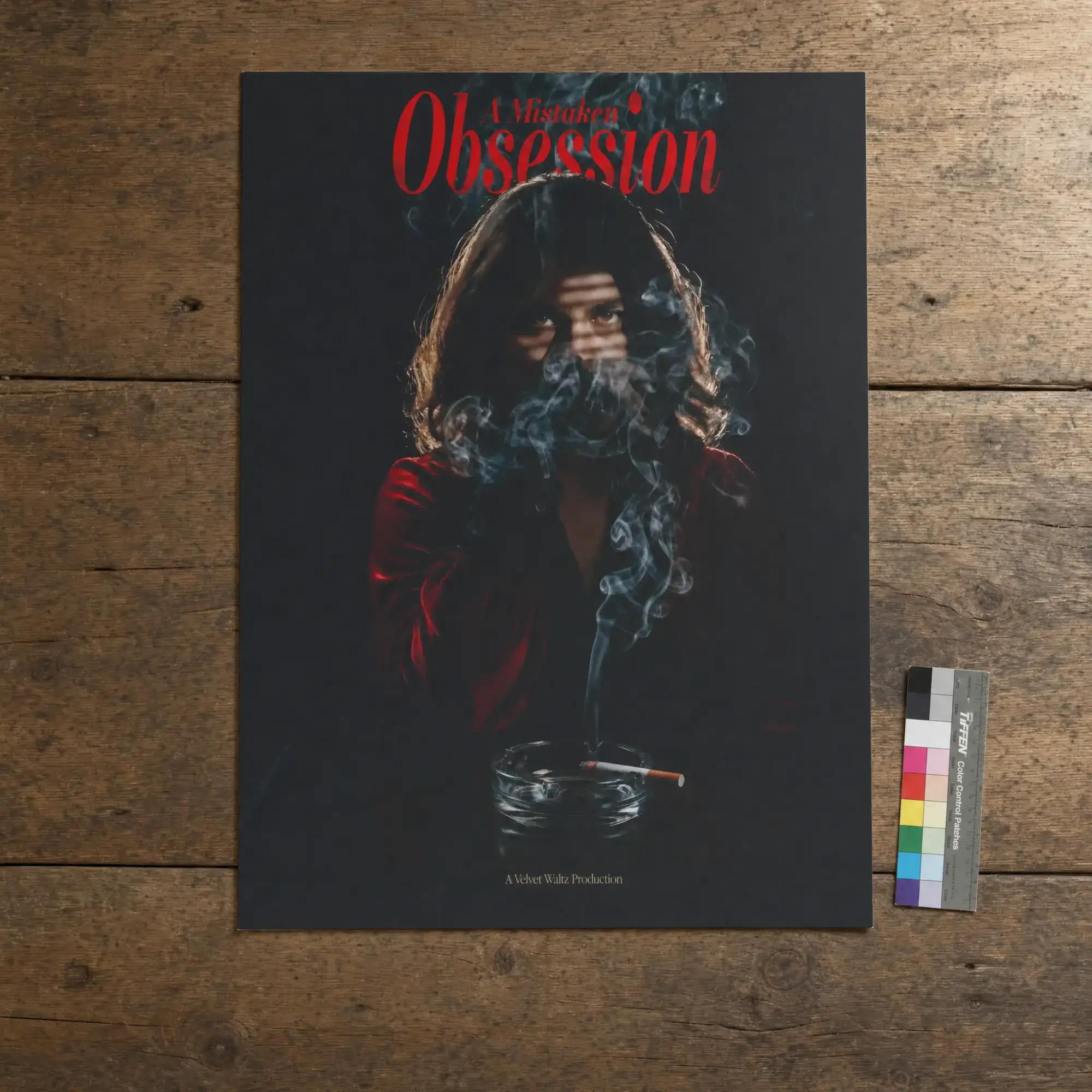 A Mistaken Obsession poster of a hooded woman in smoke, laid flat on wood with a colour chart