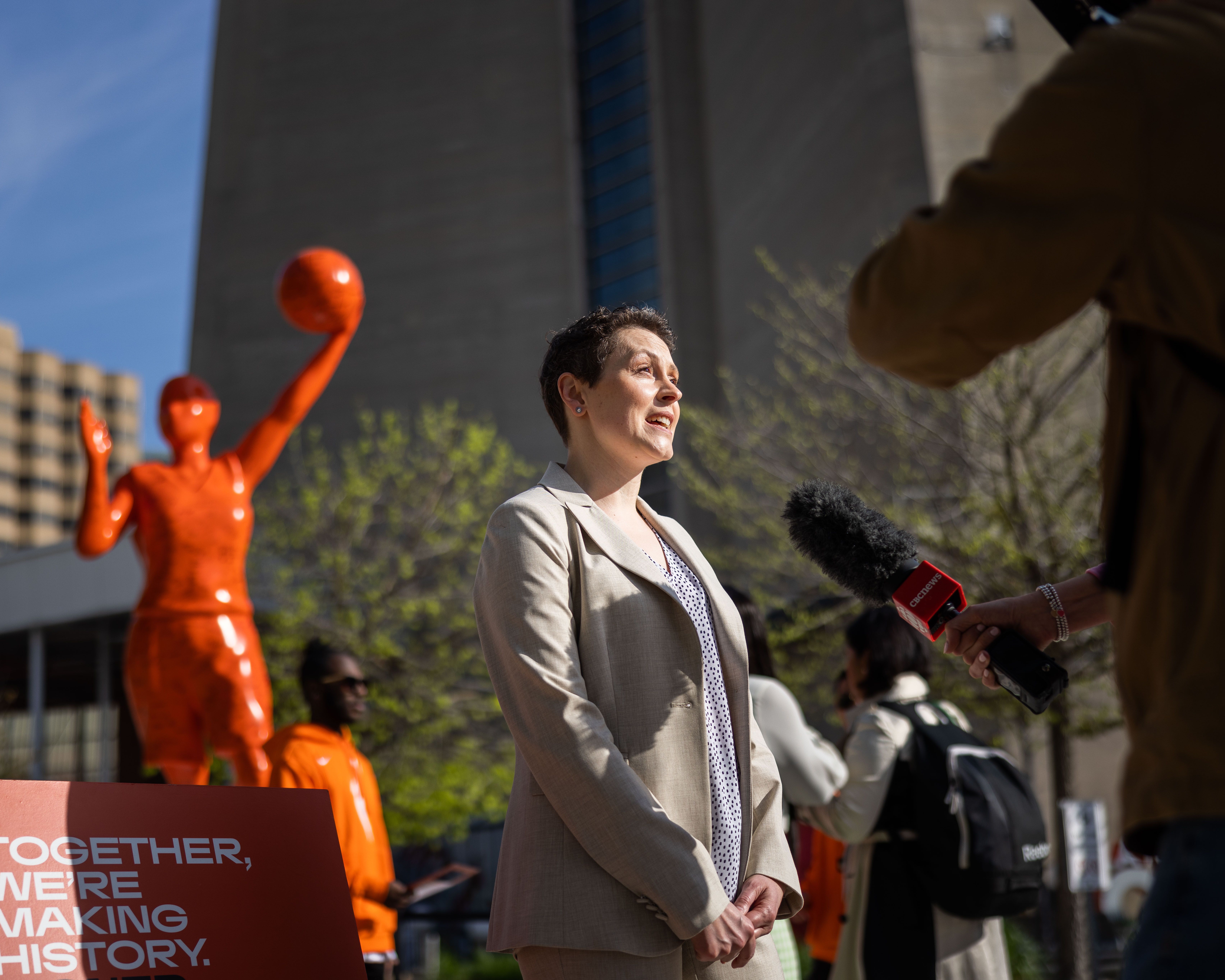 A child in a swimsuit playfully jumps with a water spray in a backyard, surrounded by toys and greenery.
