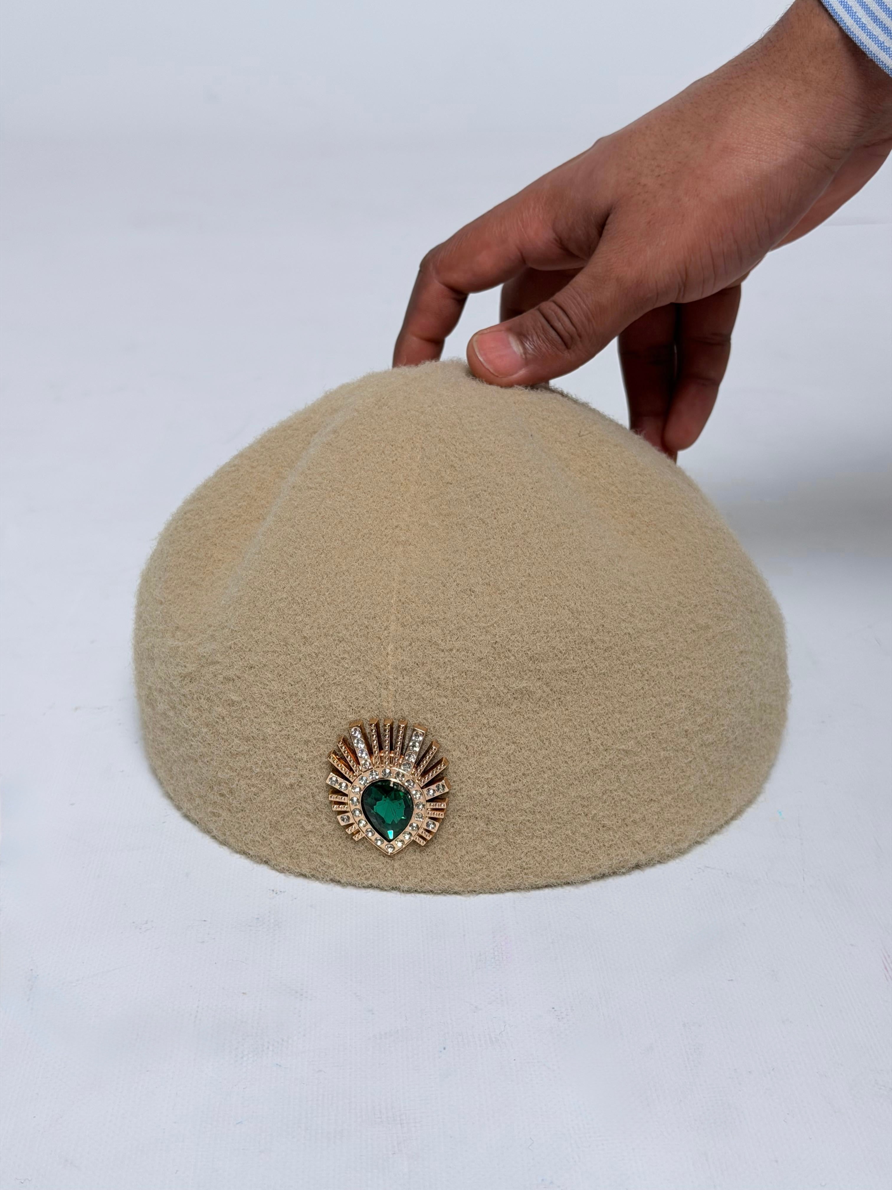 Beige decorative hat with embellishment being held.