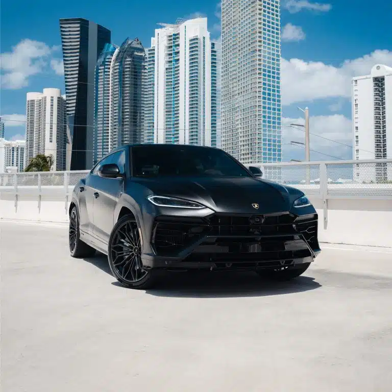 Front 3/4 view of a matte black Lamborghini Urus SE, showcasing its aggressive styling against a modern city backdrop.