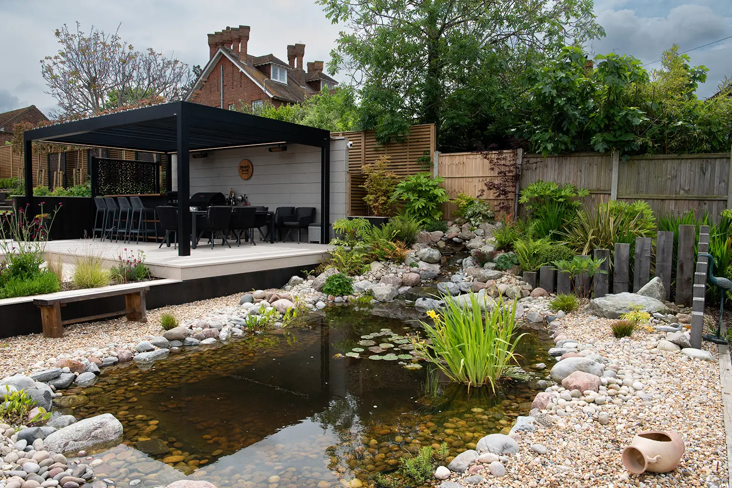 A serene garden with a pond, surrounded by greenery and a contemporary wooden structure in the background.
