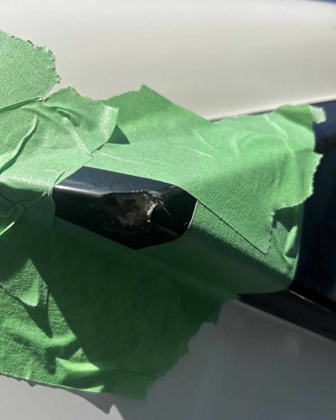 A close up of a chip in the side of a boat being taped off and repaired mid process