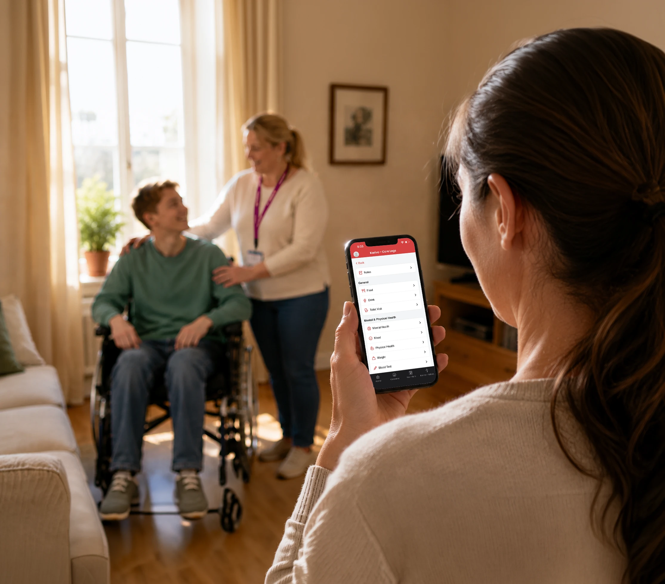 A parent checks a care app on their smartphone while, in the softly blurred background, a support carer assists her young adult child in a wheelchair in a bright, sunlit living room.