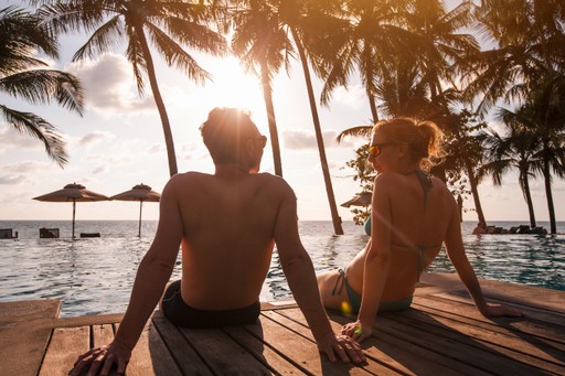 Couple holding hands while sitting on a boardwalk by the ocean at sunset.