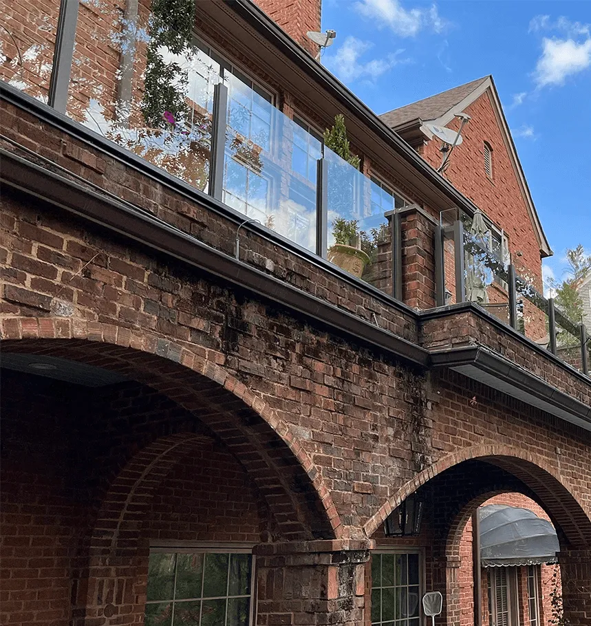 A modern wooden staircase with a glass railing, leading to an upper level, with potted plants nearby.