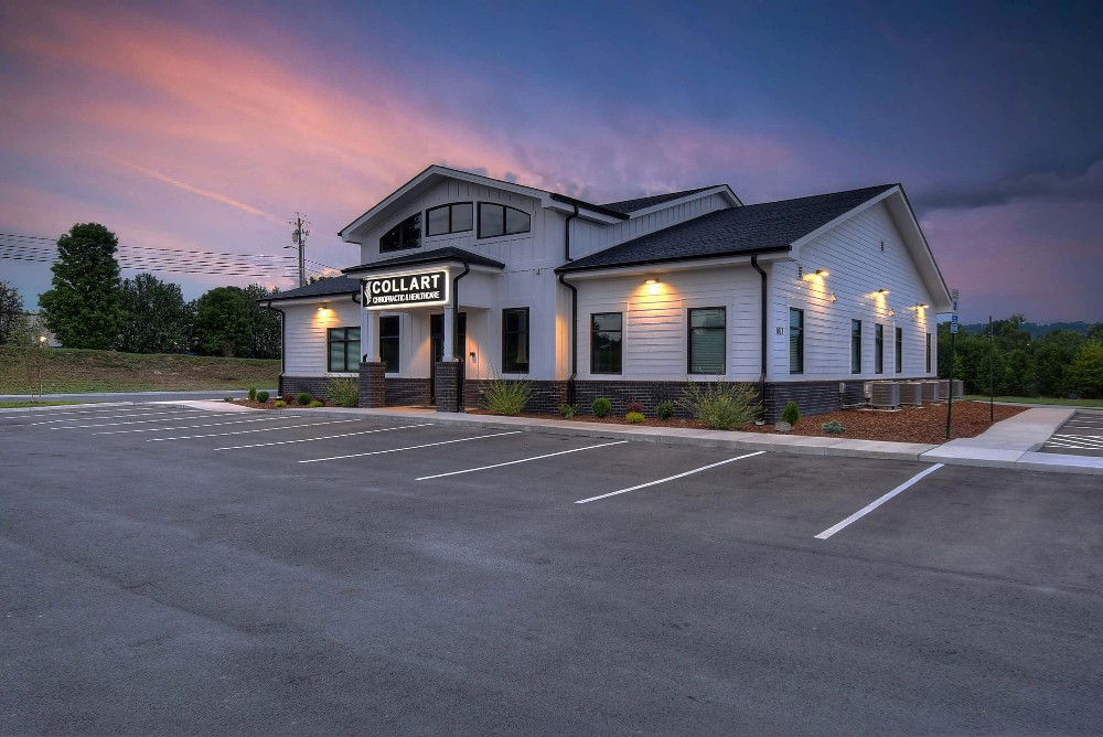 A modern building with white siding, parking space, and a colorful sunset in the background.