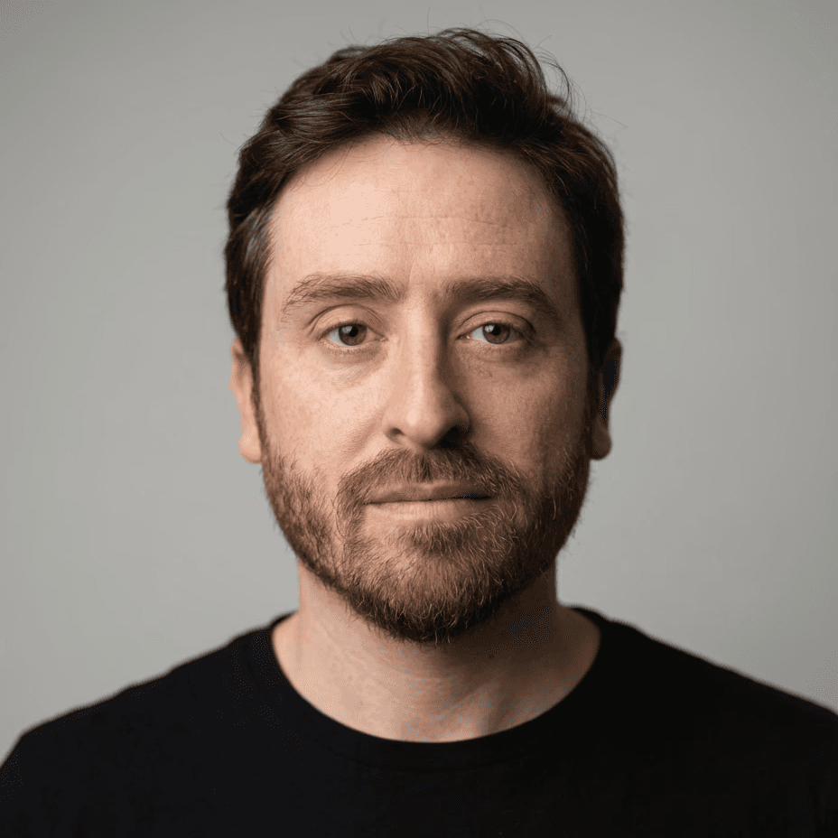 Portrait of a woman with a messy bun and hoop earrings wearing a white paint-splattered T-shirt against a gray background.