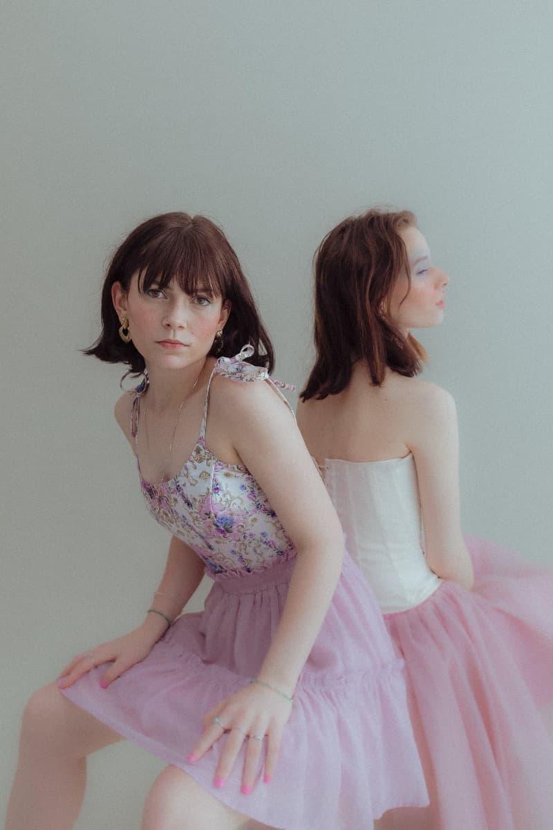 Two models sitting back-to-back, one in a floral top and pink skirt, captured in a delicate pose during a creative photoshoot at Revelator Studio in Shreveport.