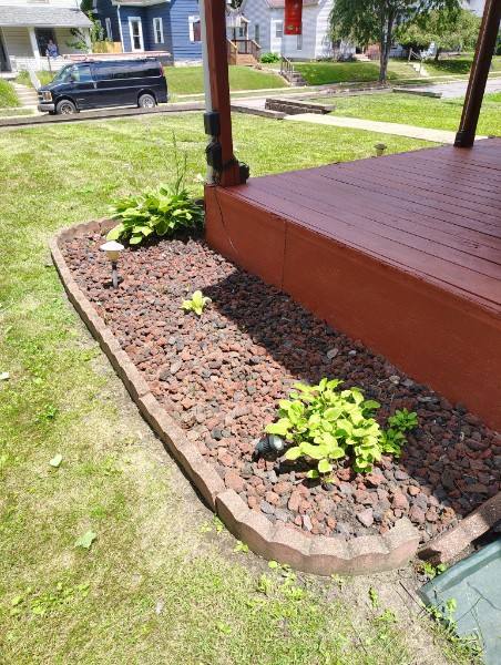 Red lava rock landscape bed with scalloped stone edging and plantings around a deck in Madison County, Indiana