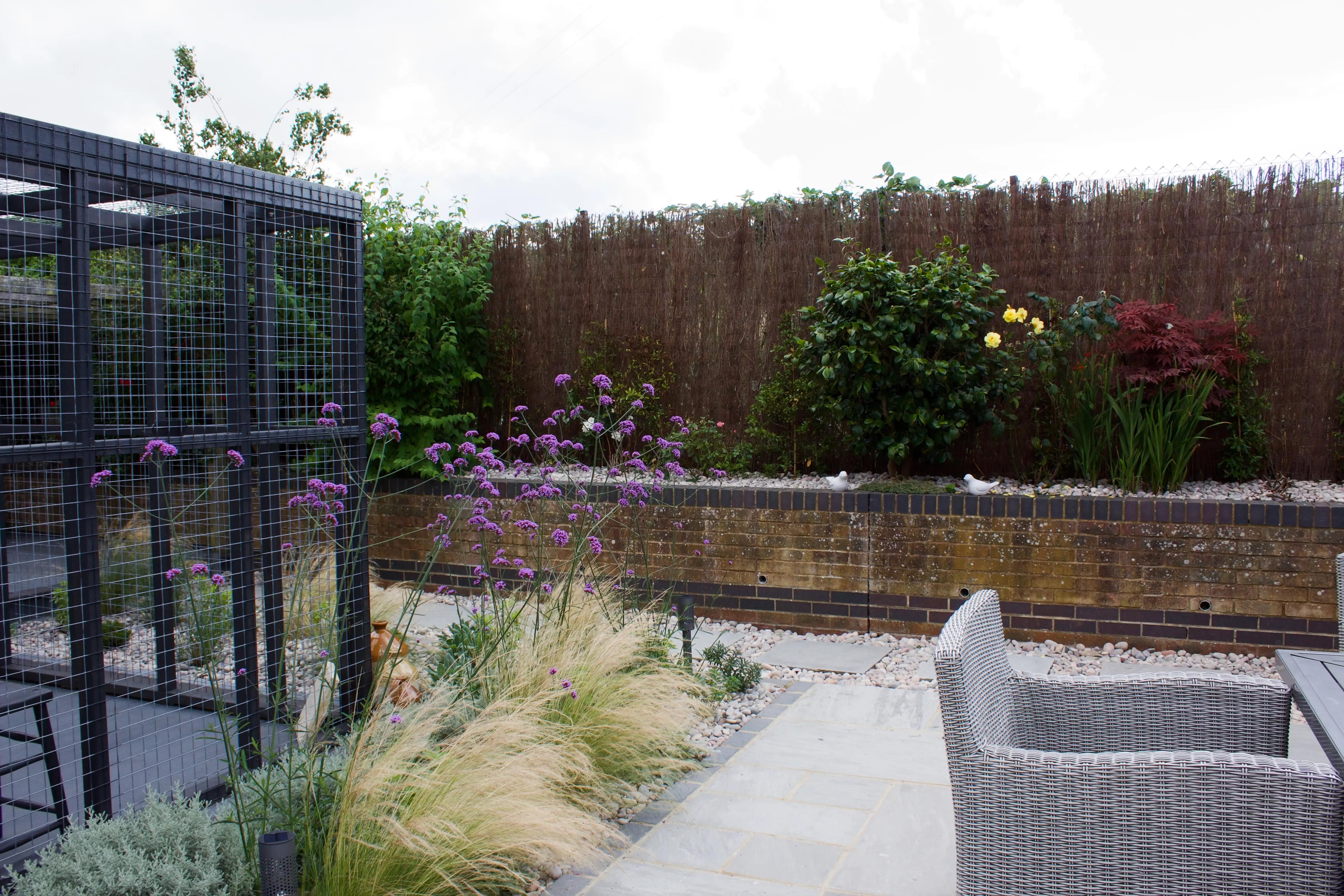 A modern outdoor patio with potted plants, a stone pathway, and a wooden fence in the background under a cloudy sky.
