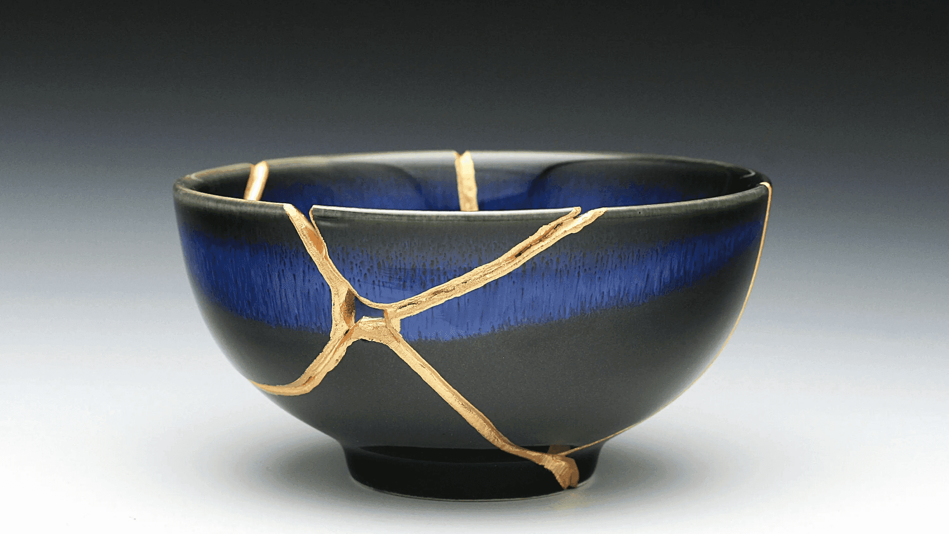 Kintsugi bowl with gold-filled cracks on a dark blue and black glaze, symbolizing strength and beauty found through breakage and repair.