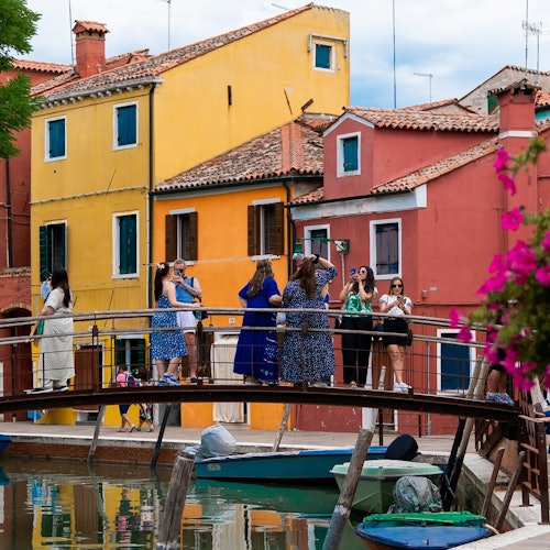 一群人站在运河上的一座小桥上,背景是色彩缤纷的房屋和船只。