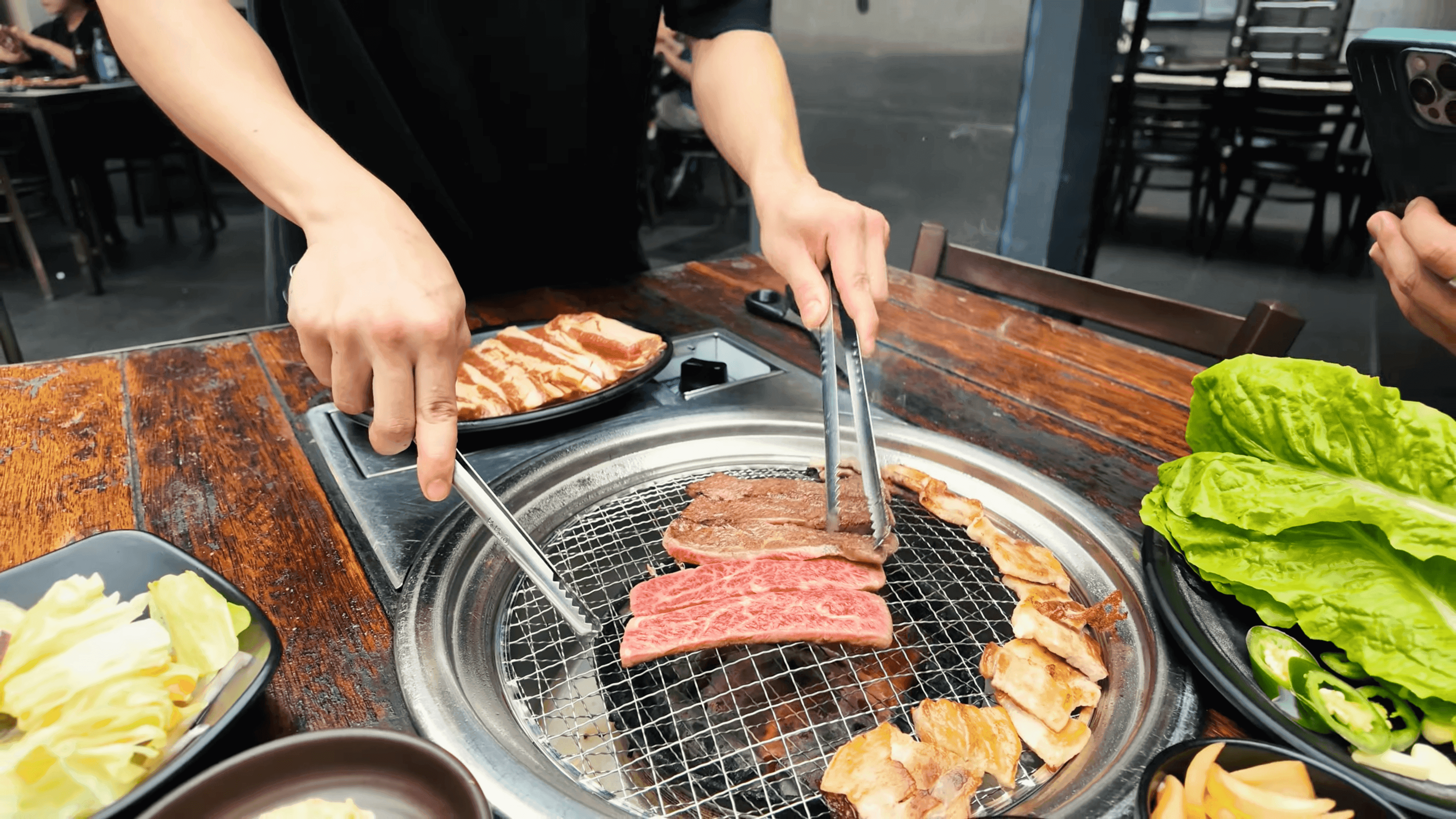 Four pieces of fried chicken or battered fish on a bed of salad greens, being heavily topped with shredded white cheese that is raining down onto the dish, set against a dark, rustic background of wood and pine cones.