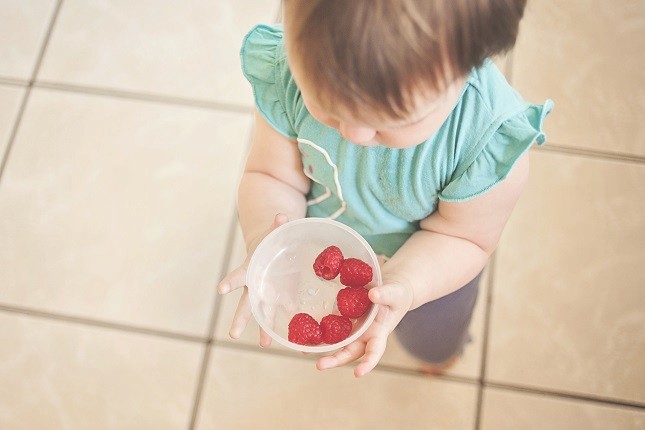 dziecko trzymające plastikową miseczkę pełną malin