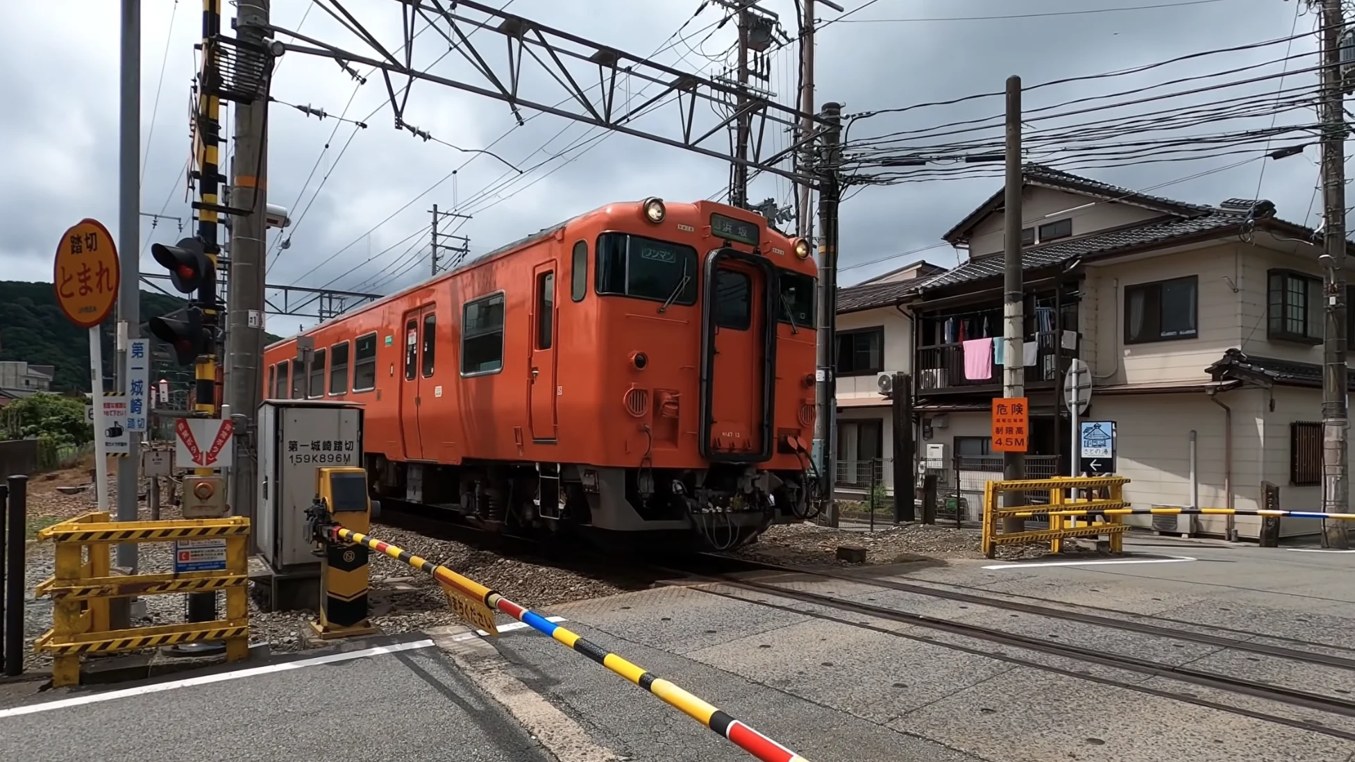 A red railcar waiting at a level crossing on a residential street near Kinosaki.