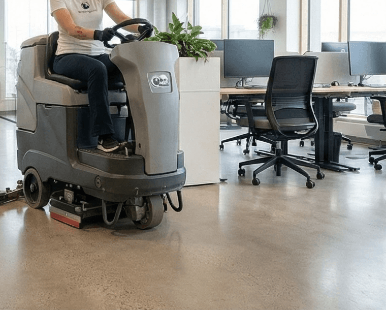 Starfsmaður á gólfþvottavél að þrífa stóran gólfflöt á vinnustað.