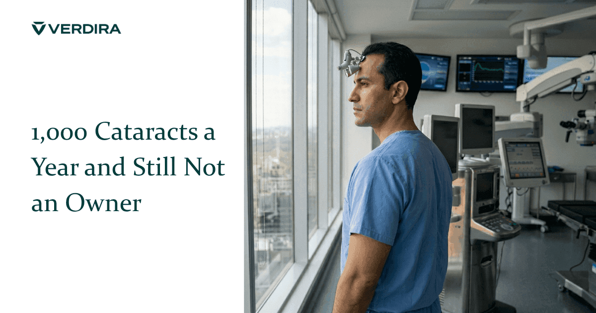 Young male ophthalmologist in surgical scrubs and loupes standing in operating room looking out window
