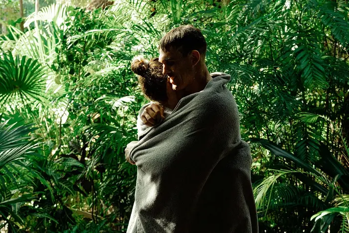 Pareja abrazándose y secándose con una toalla después de nadar, rodeados de árboles pequeños en la jungla en Nômade Tulum, México.