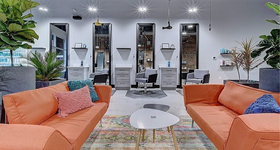 A modern lounge area featuring orange sofas, a coffee table, decorative plants, and stylish wall decor.