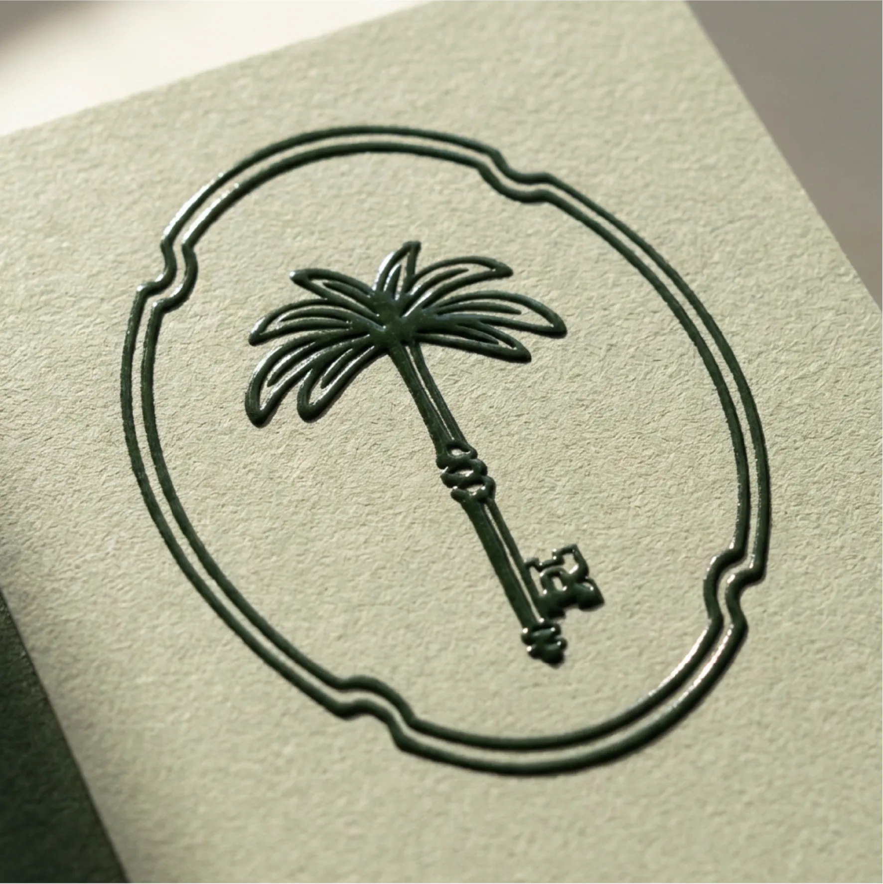 The emblem palm-key logo is printed in deep green ink, in a raised glossy way on a sage green card.