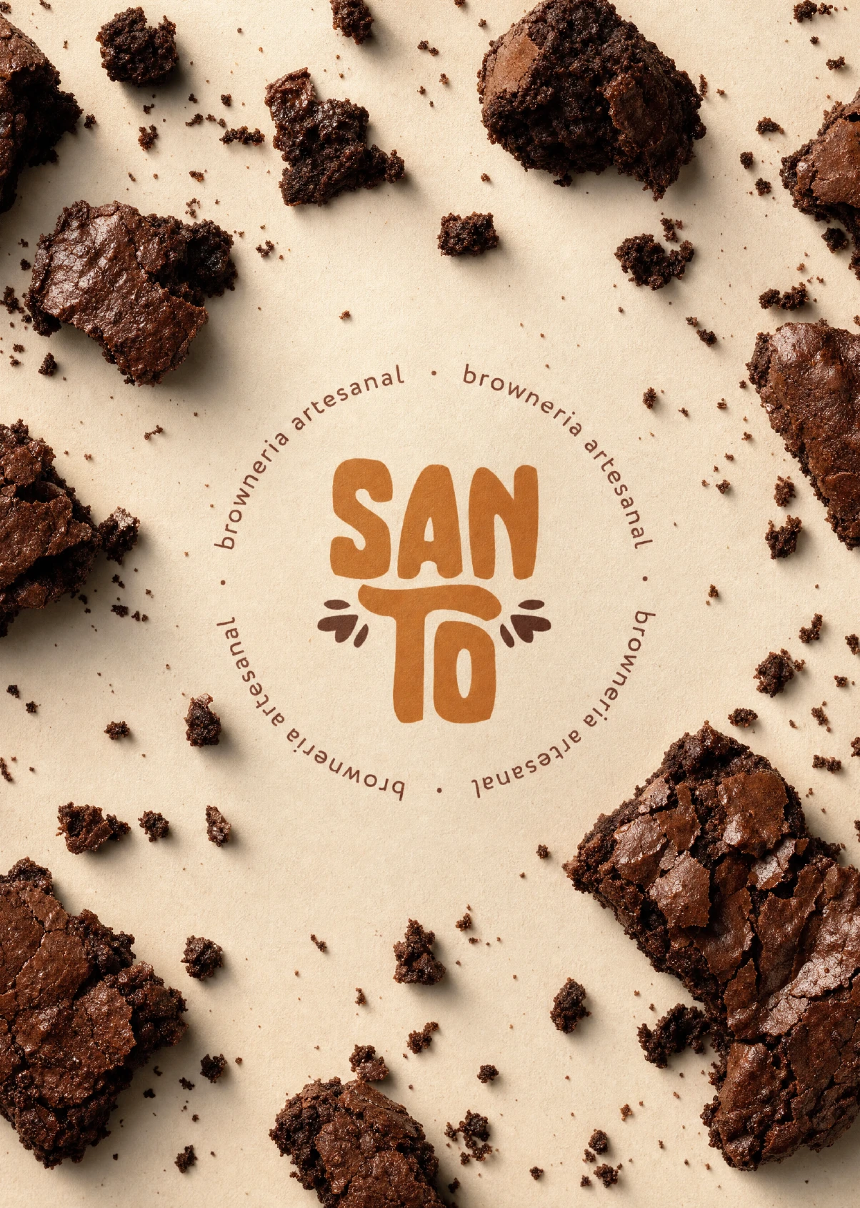 Circular Santo Brownie emblem on beige paper surrounded by scattered brownie chunks, with "SANTO" in orange script lettering and "browneria artesanal" repeated around the ring.