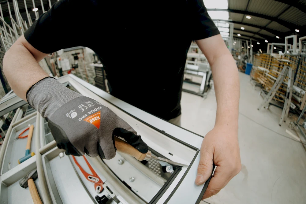 Ein Arbeiter montiert ein Fensterrahmen mit einem Werkzeug. Nahaufnahme der Hände mit Handschuh.