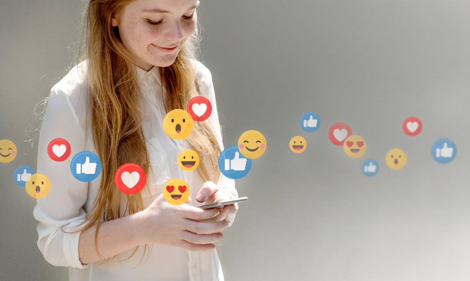  A woman holding a cell phone displaying various colorful emojis on the screen, smiling as she interacts with it.