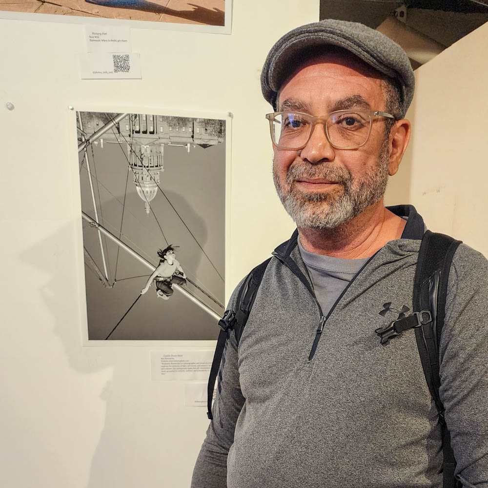 Benjamin Hernandez standing next to a framed photograph on exhibition at a gallery.