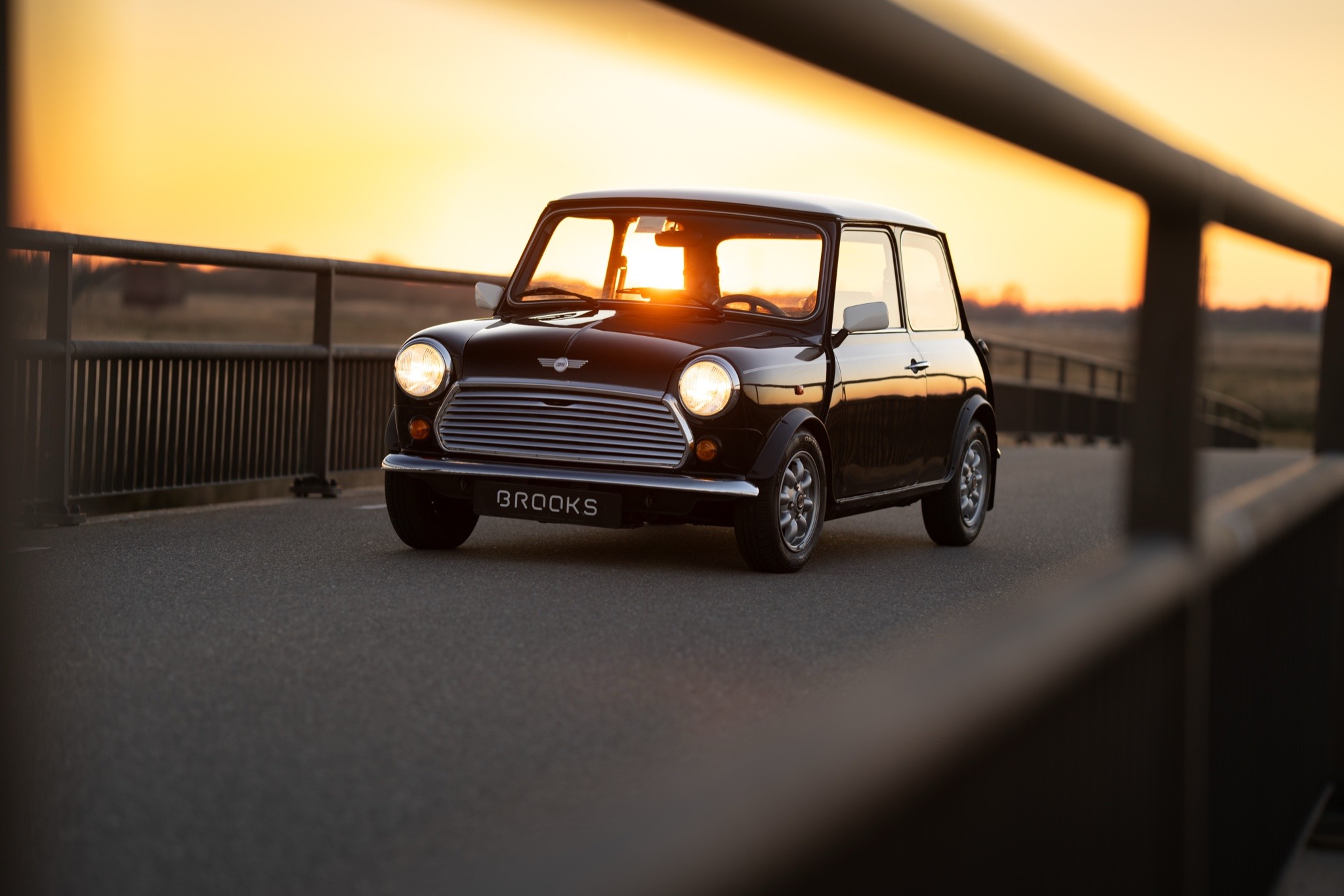 Mini Cooper S Pack Conversion, a 1991 classic Mini Cooper S conversion, black with white roof, lit up on a sunset bridge