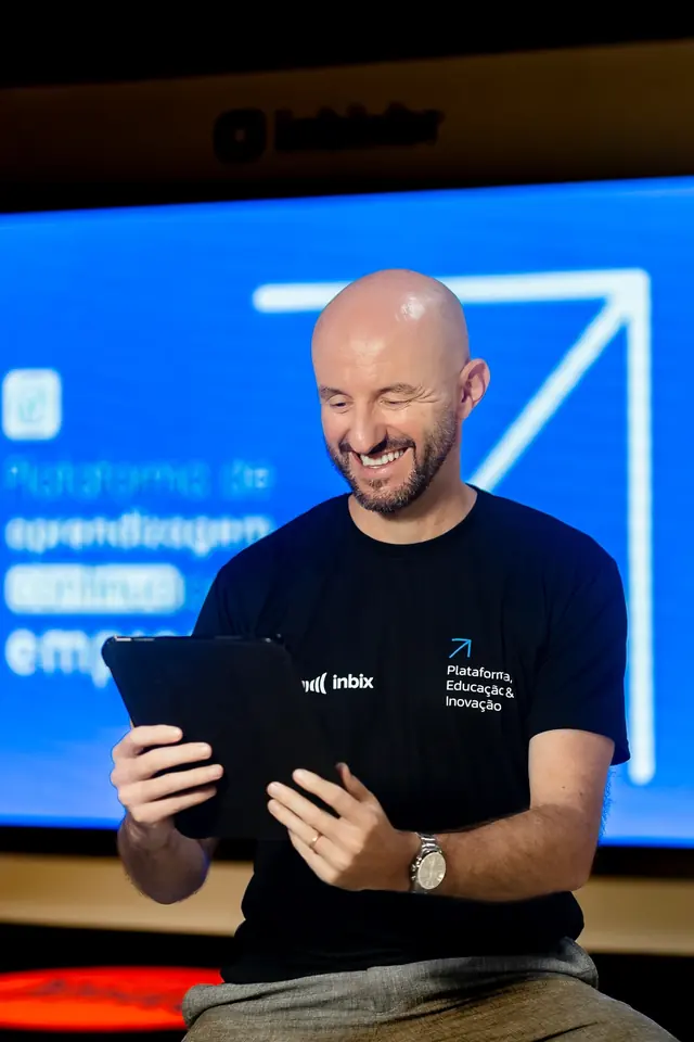 Man smiling and holding tablet, wearing Inbix t-shirt. Blue text in background highlights "Plataforma de Educação & Inovação".