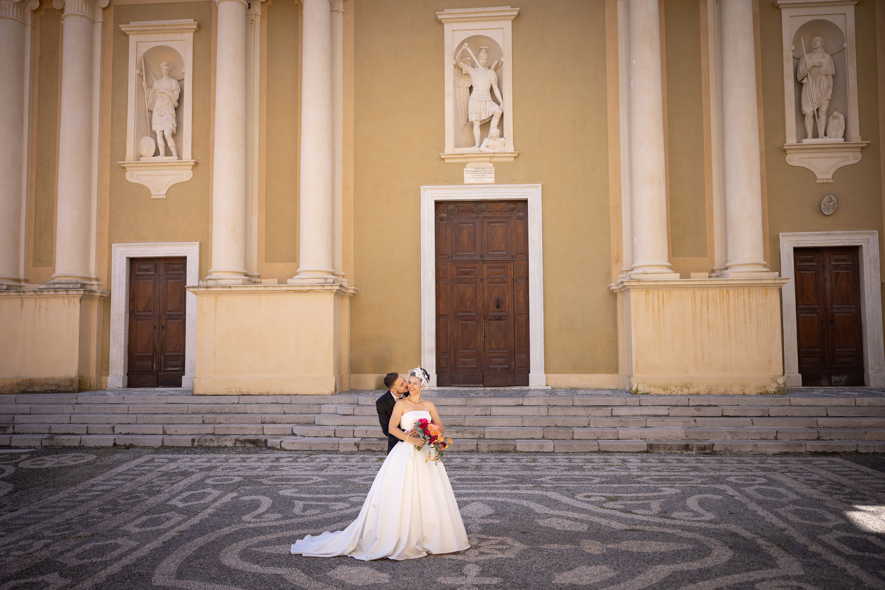 photographe-mariage-menton Sur l'esplanade de l'église, un couple amoureux s'embrasse