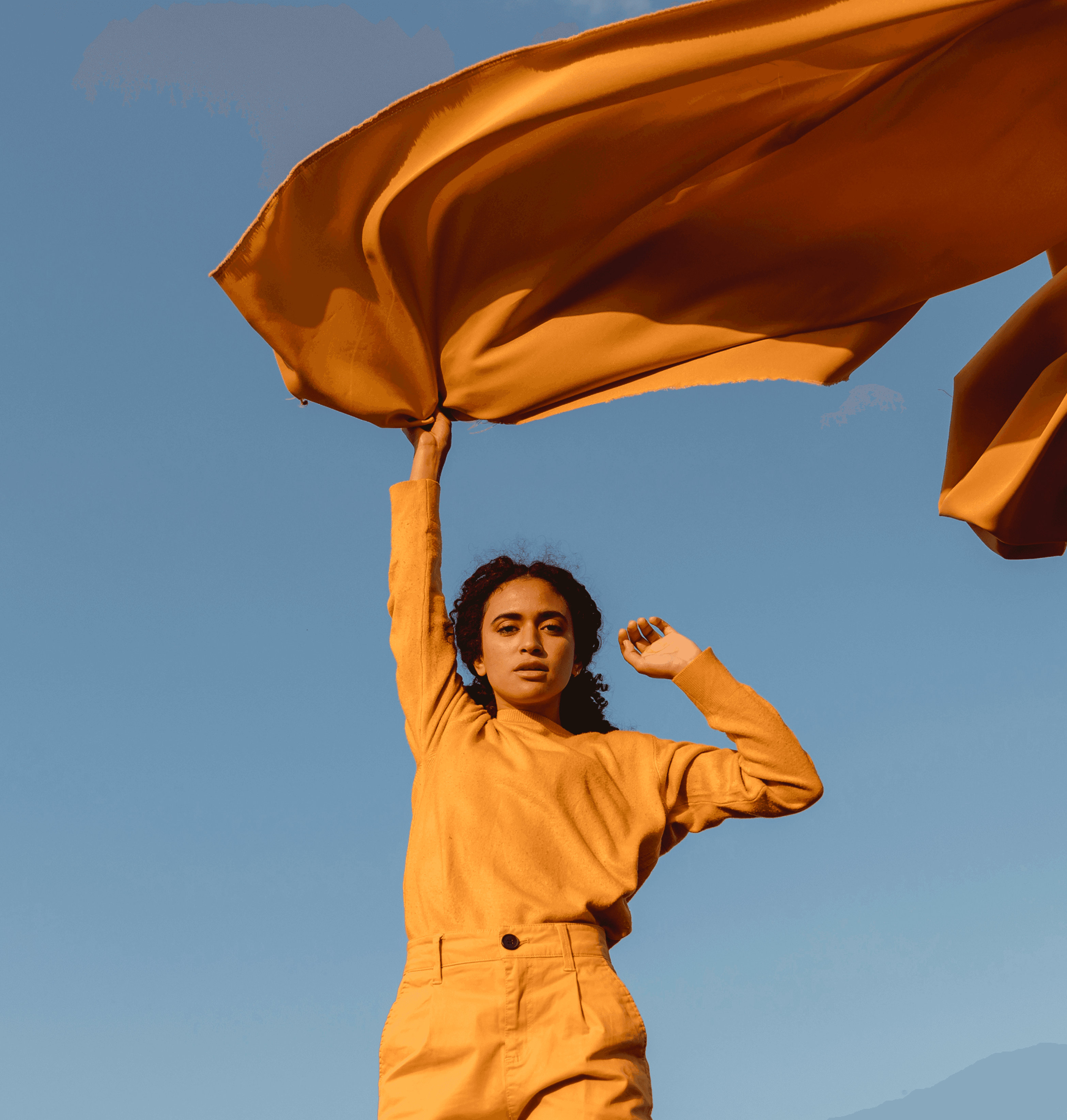 Woman in yellow outfit holding yellow fabric against blue sky