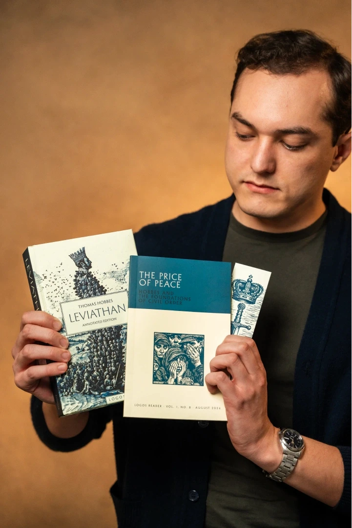 A woman with long hair and a black blazer holds a copy of Boethius's "The Consolation of Philosophy" next to her face, published by Logos.