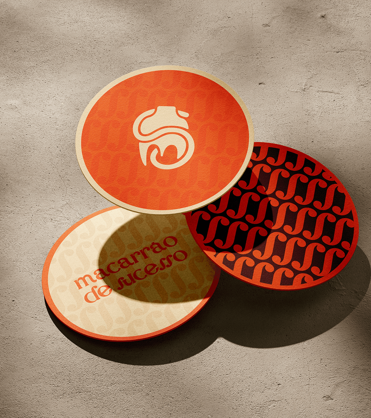 três porta copos sobre um chão de concreto, em cada um dos elementos, grafismos e ativos visuais da marca macarrão de sucesso são exibidos.
