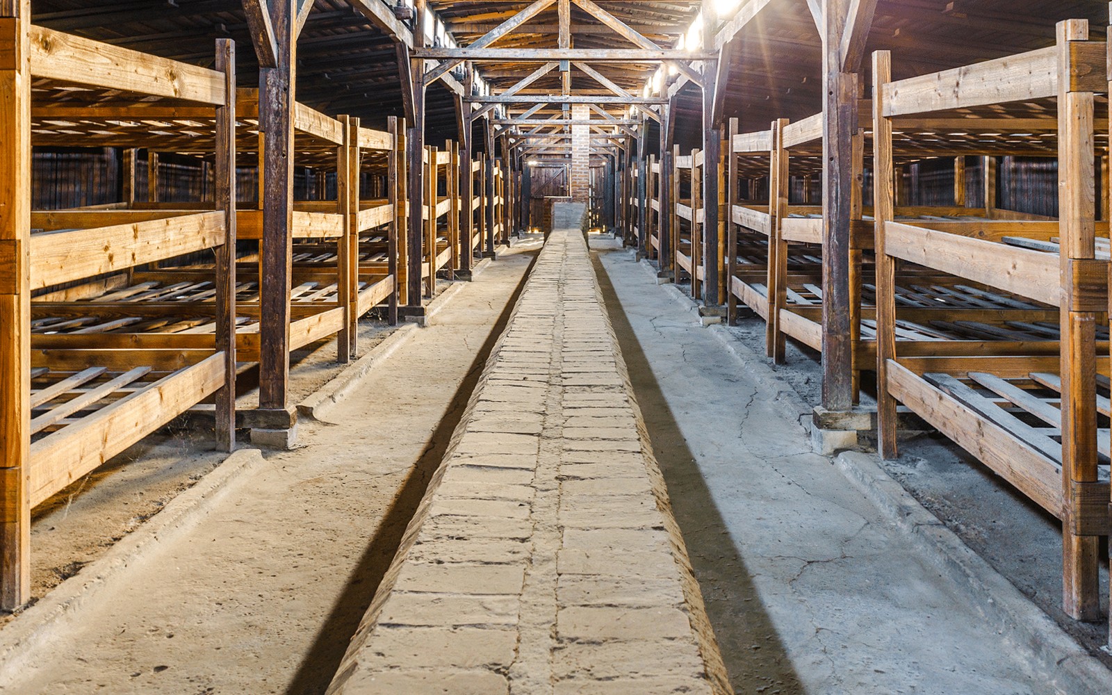 Interior de los barracones de Auschwitz Birkenau con literas de madera y pasillo central.