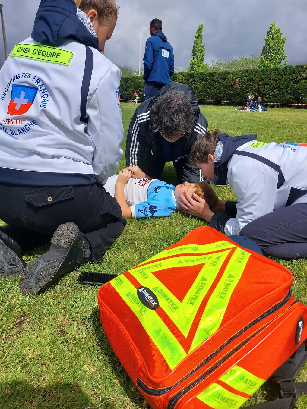 Secouristes français aidant un enfant sur un terrain de sport avec équipement médical d'urgence.