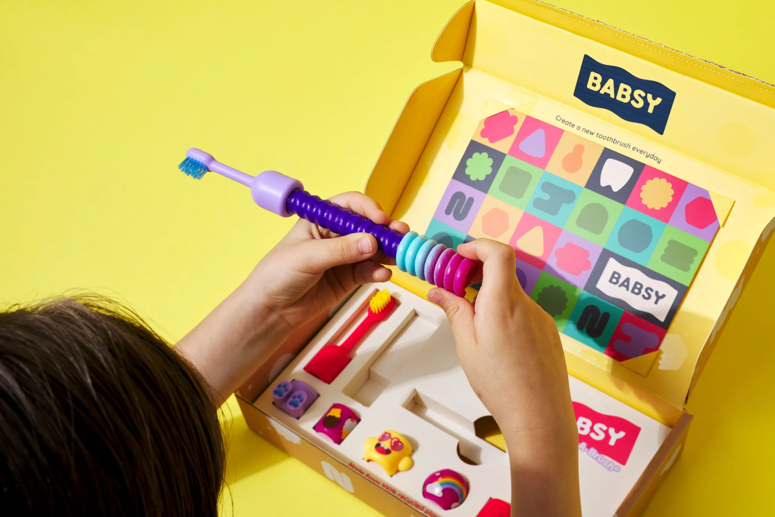 Child assembling a colorful BABSY Build-A-Brush toothbrush from the open activity kit