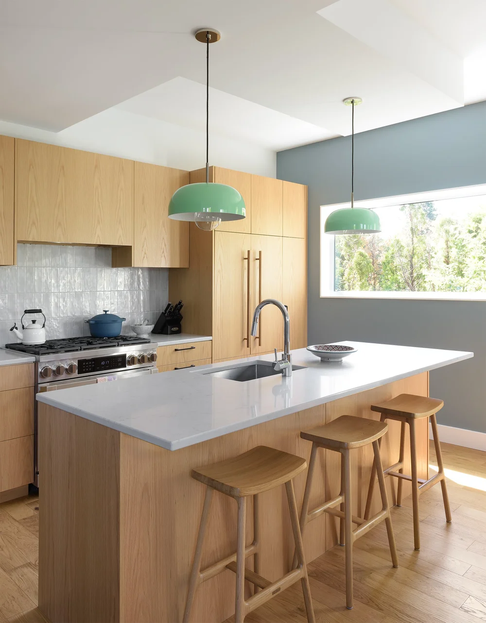 Modern two-story home with large glass windows, warmly lit interiors, and a balcony. Surrounded by trees and a manicured lawn at dusk. Cozy ambiance.