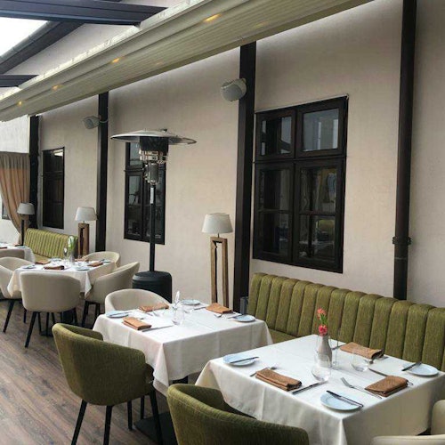 户外餐厅座位区设有绿色椅子、白色桌布、餐具、玻璃门和暖炉。