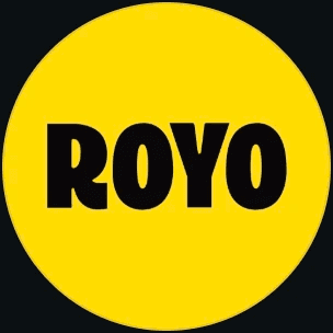 A woman with blonde bob hair in a grey coat and beige turtleneck stands against a neutral backdrop. She has a serious expression, conveying elegance.