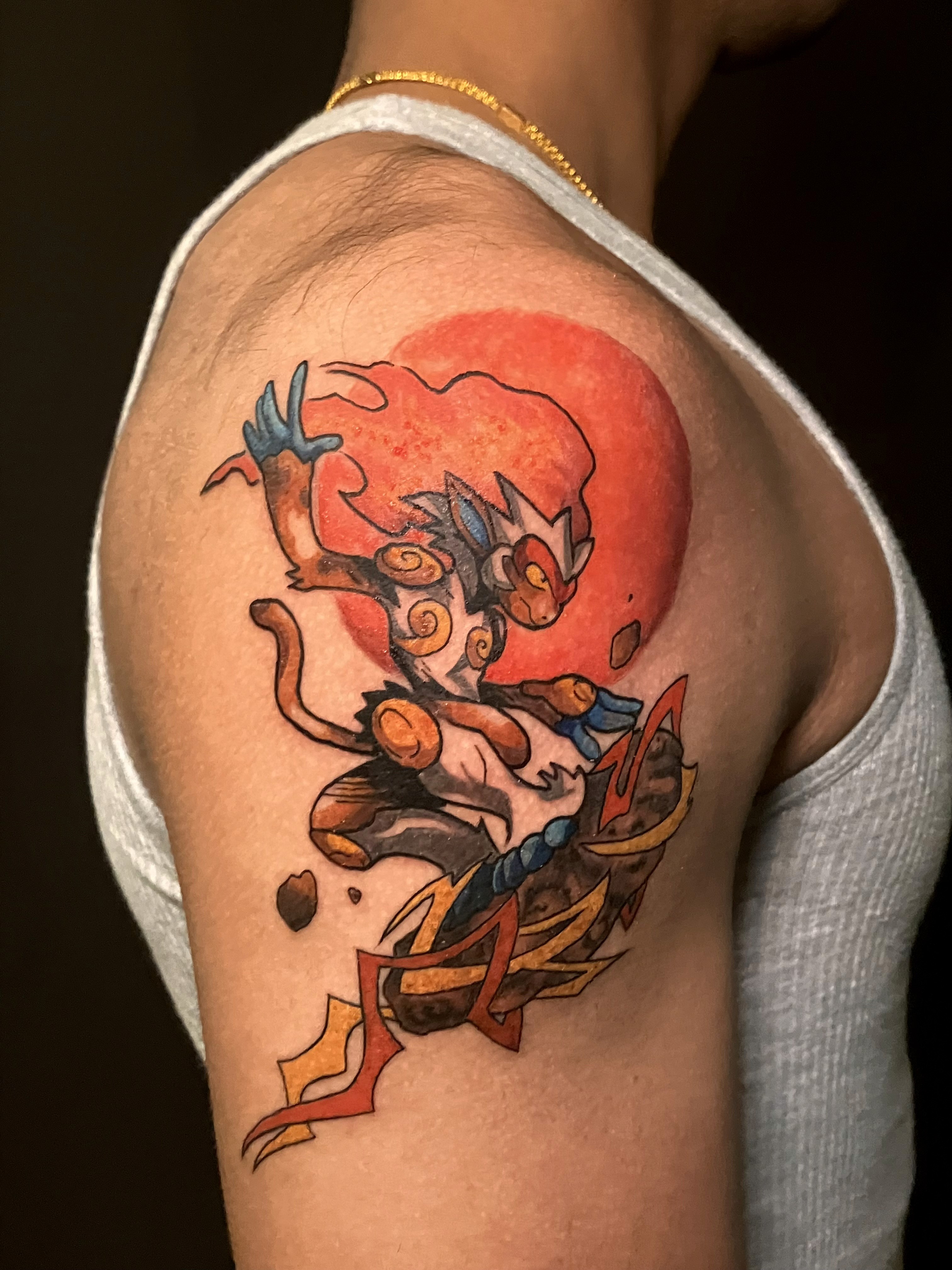 A vibrant tattoo of a chainsaw-like creature on a person's forearm. The tattoo is detailed with shades of orange, black, teal, and red.