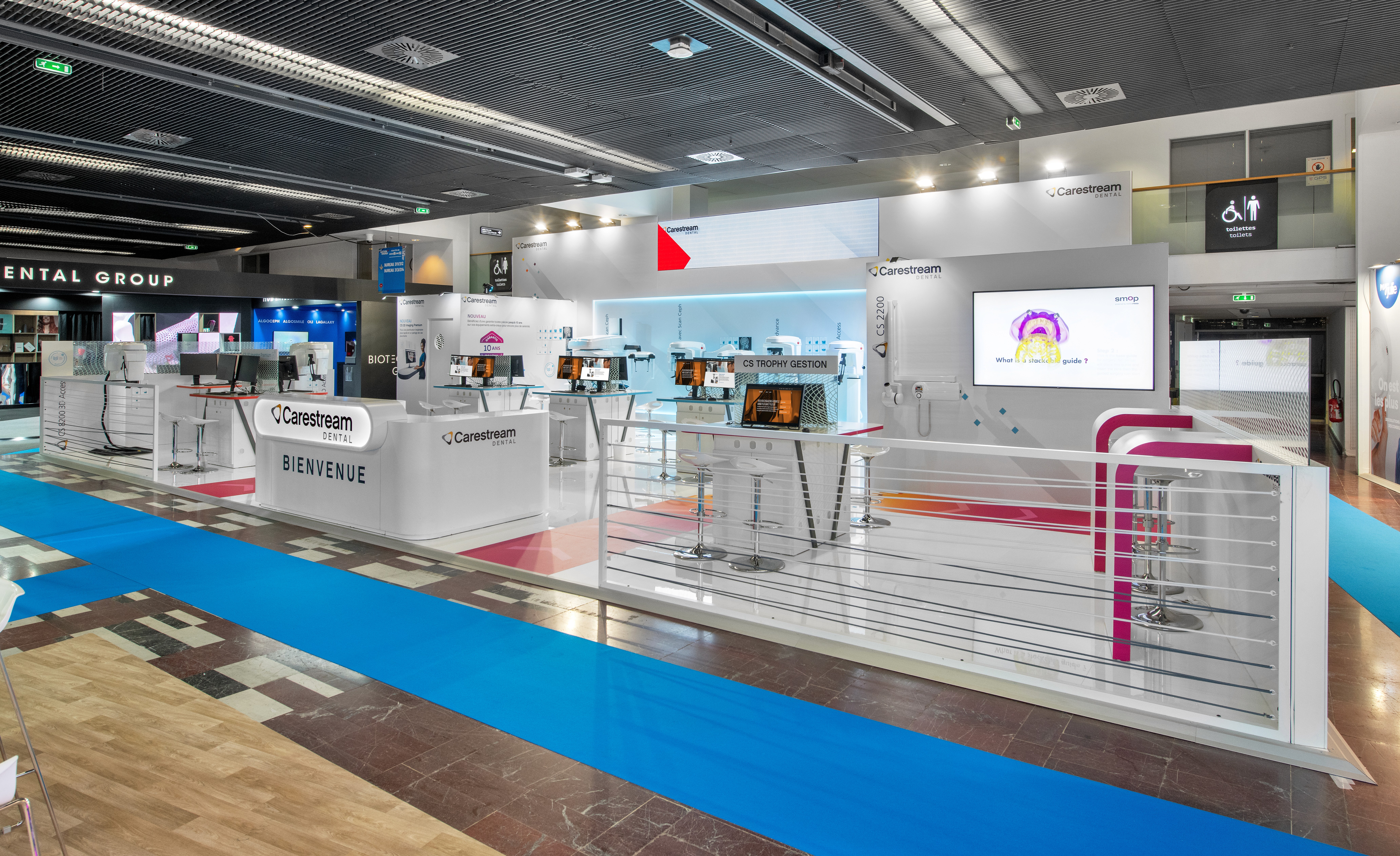 Stand Carestream Dental congrès ADF réalisé par Expace – vue intérieure avec mur d'imagerie dentaire rétroéclairé bleu, gamme CS 9600 Scan Ceph et postes de démonstration logiciel CS Trophy Gestion