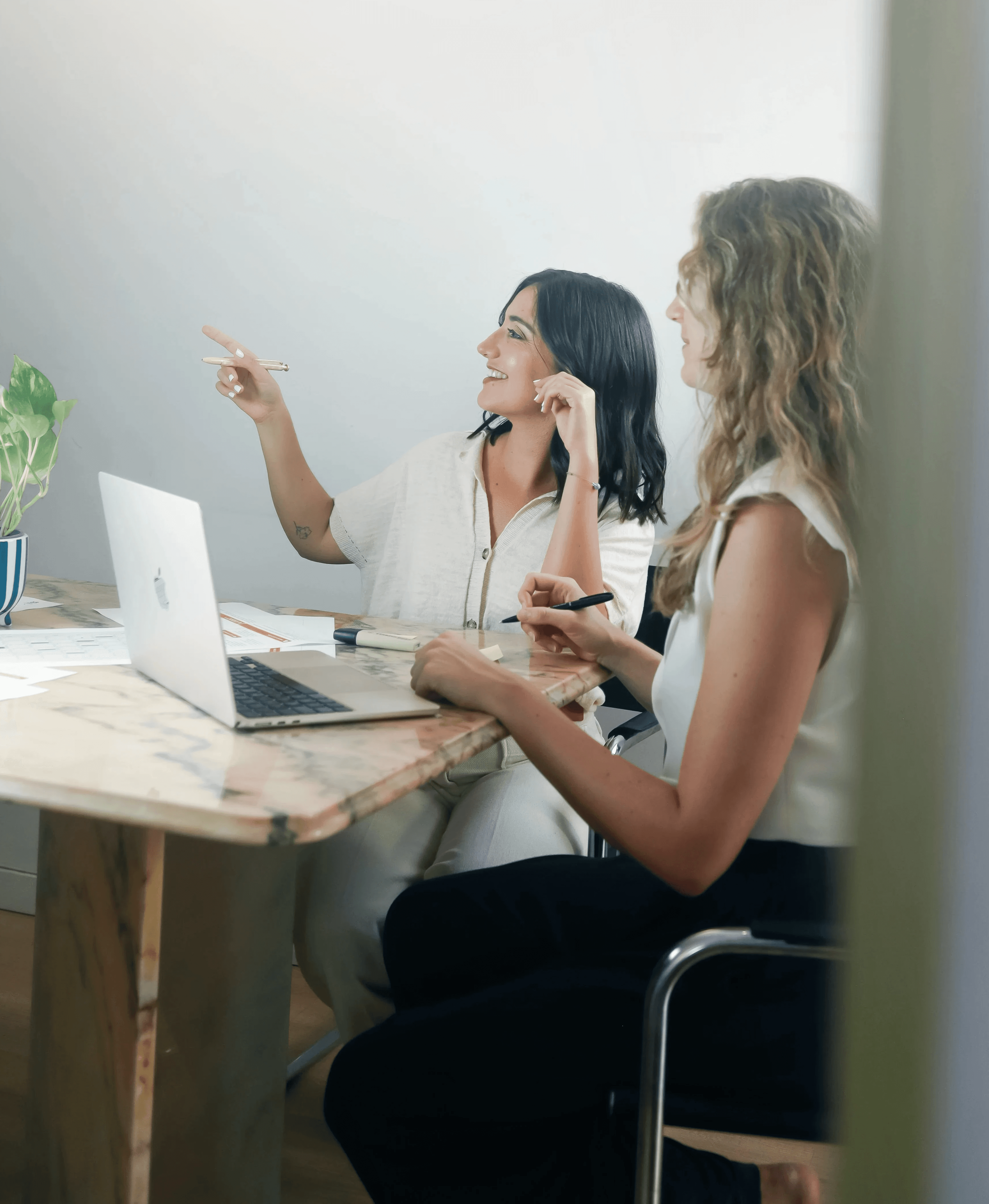 Two colleagues collaborating at a desk, reviewing project materials and pointing at a laptop during a strategy session
