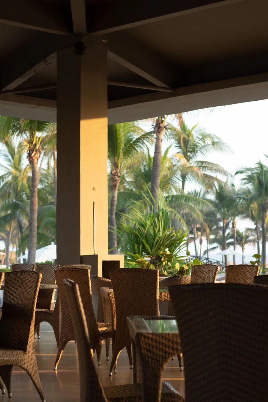 Open-air resort restaurant and bar with casual dining tables and tropical plants.
