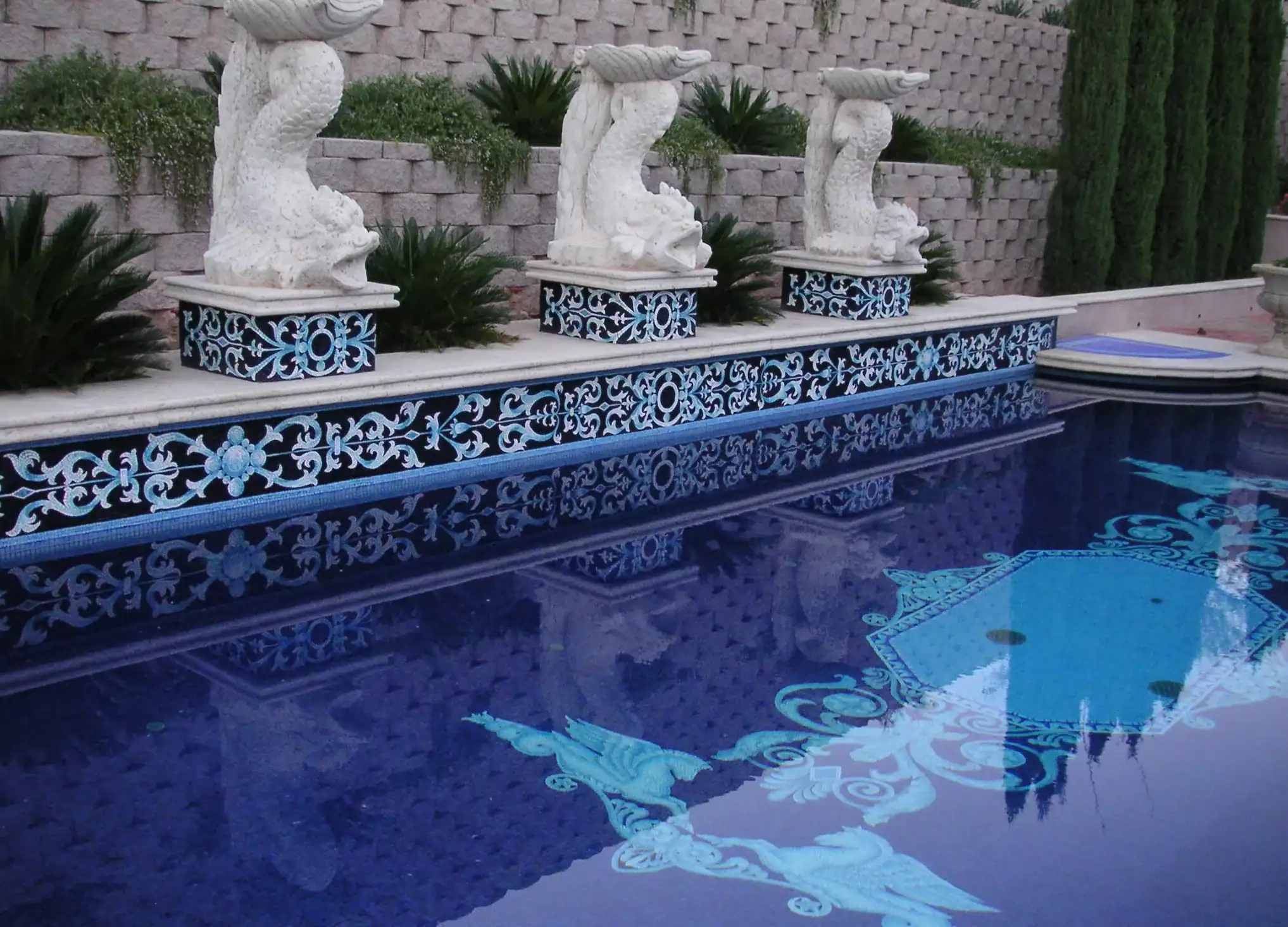A swimming pool with winged hippocampi set into its floor, an ornate blue and white Venetian border at the waterline, and three matching hippocampus figures standing along the coping.