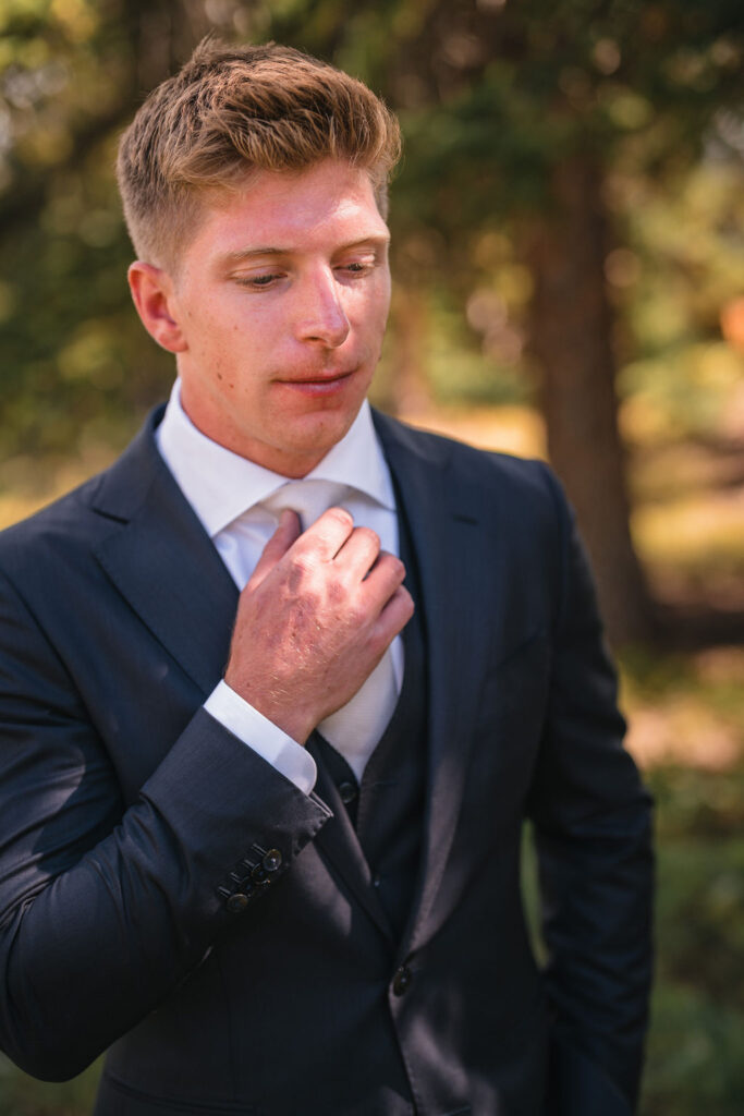 Groom fixing tie in forest setting at Smith Cabin Aspen wedding preparation moments
