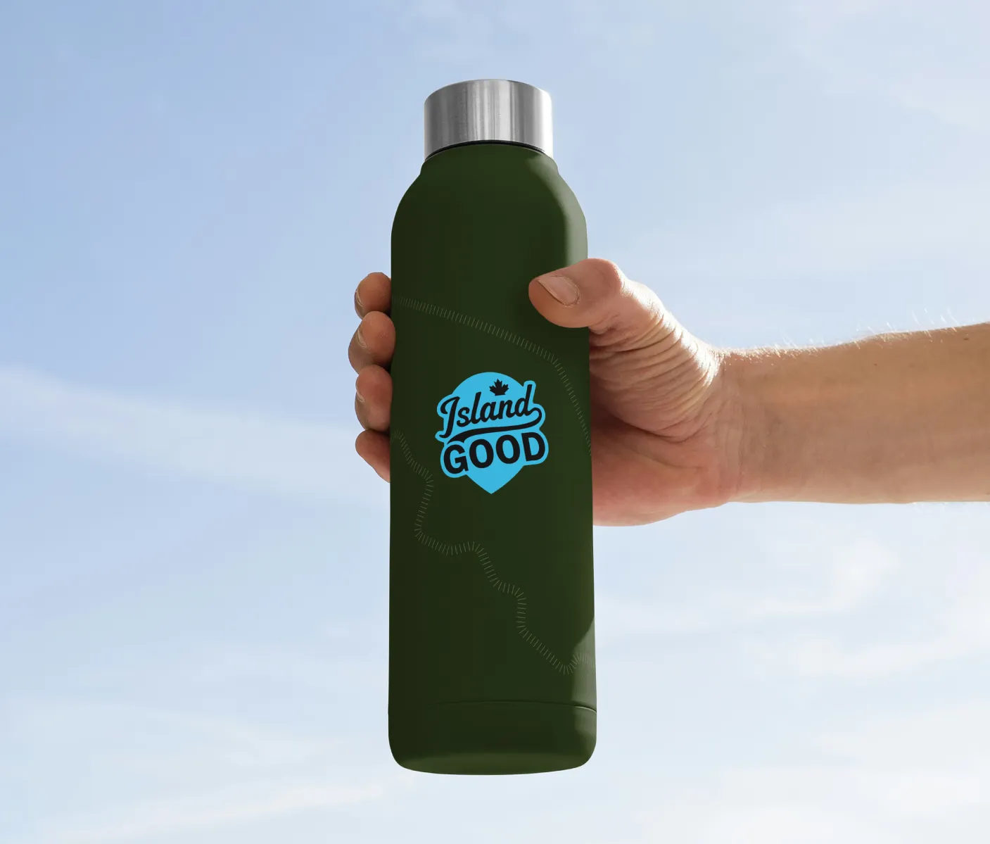 A blue Island Good logo on a forest green water bottle being held by a hand with the sky in the background.